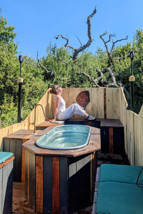 Guest relaxing in the wood-fired hot tub trailer beside the Vacationist eco-cabin in Sussex