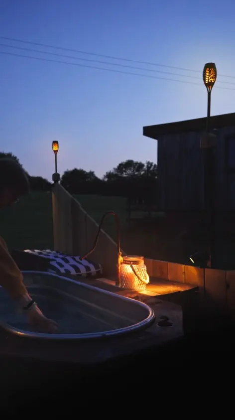 Wood-fired hot tub at dusk with lanterns and torchlight at a secluded Sussex glamping cabin