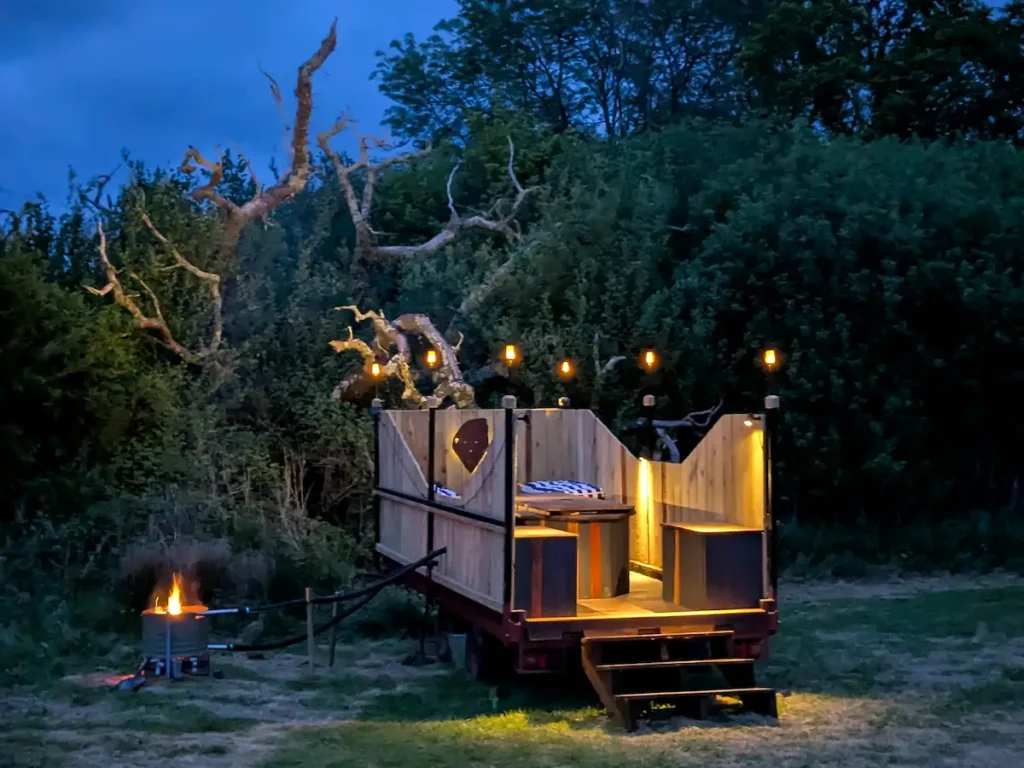Wood-fired hot tub trailer lit at night beside a private cabin in Sussex