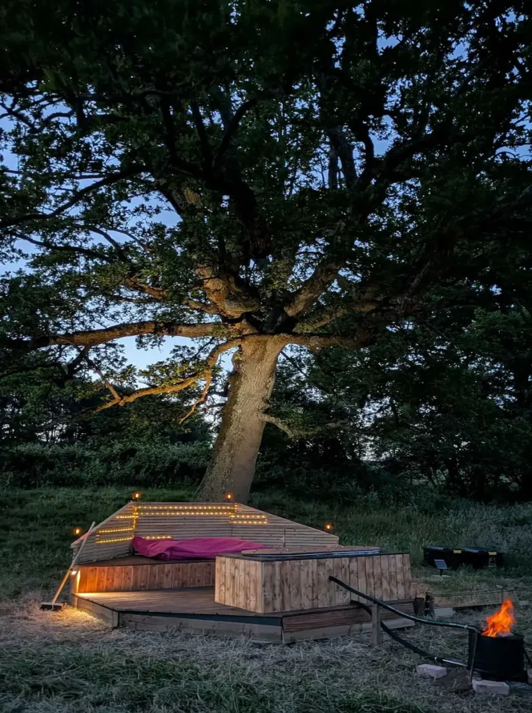 Wood-fired hot tub at Skoolie Stays glamping accommodation in West Sussex beneath a large oak tree